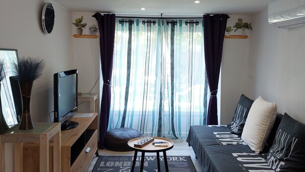 A modern living room with a TV, sofa, and a rug with city names. - Le Petit Jules (Agen)