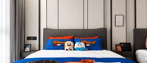 A hotel room with a bed featuring cartoon character bedding, a grey headboard, and a nightstand with a lamp.