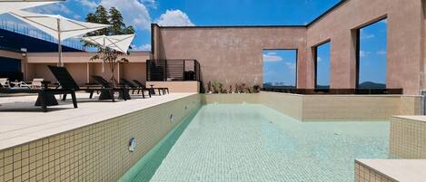 A rooftop pool with tiled walls, lounge chairs, and umbrellas.