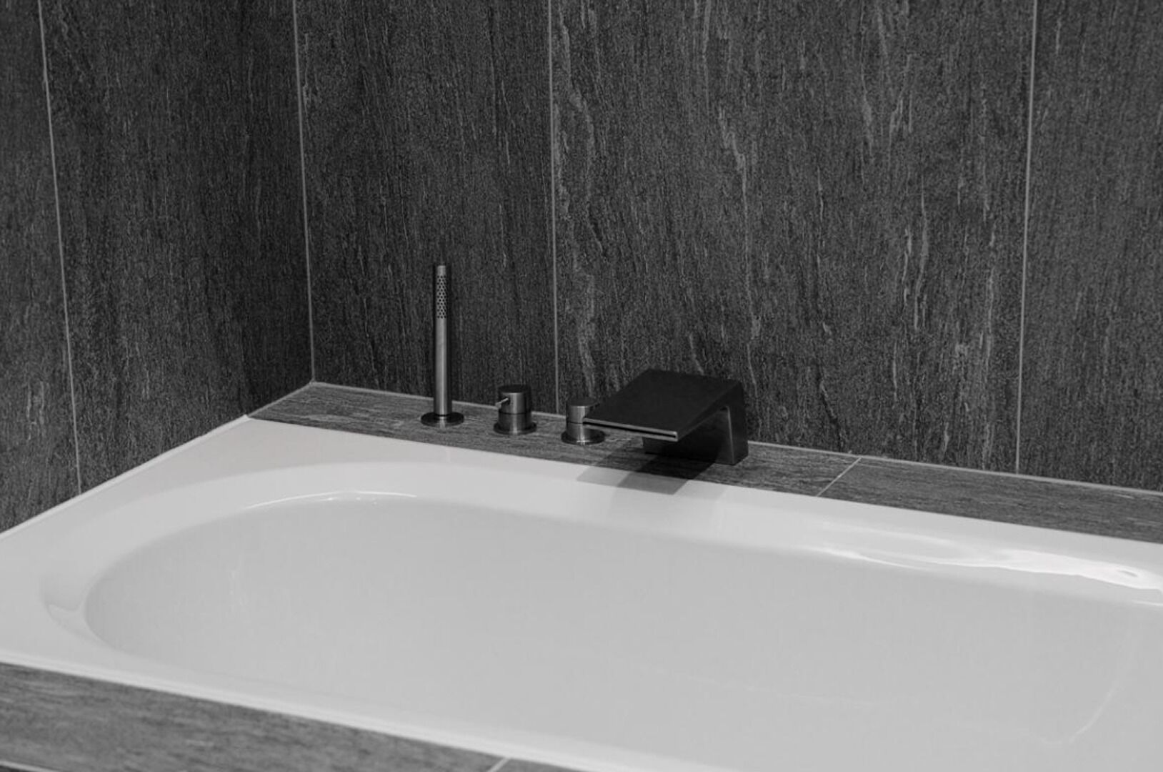 Un baño moderno con una bañera independiente, un cabezal de ducha manual y un toallero negro.