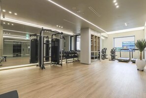 A modern gym with exercise equipment, a large mirror, and a view of a building through the window. - Daegu Suseong The Arco Hotel Lions Park (Daegu)