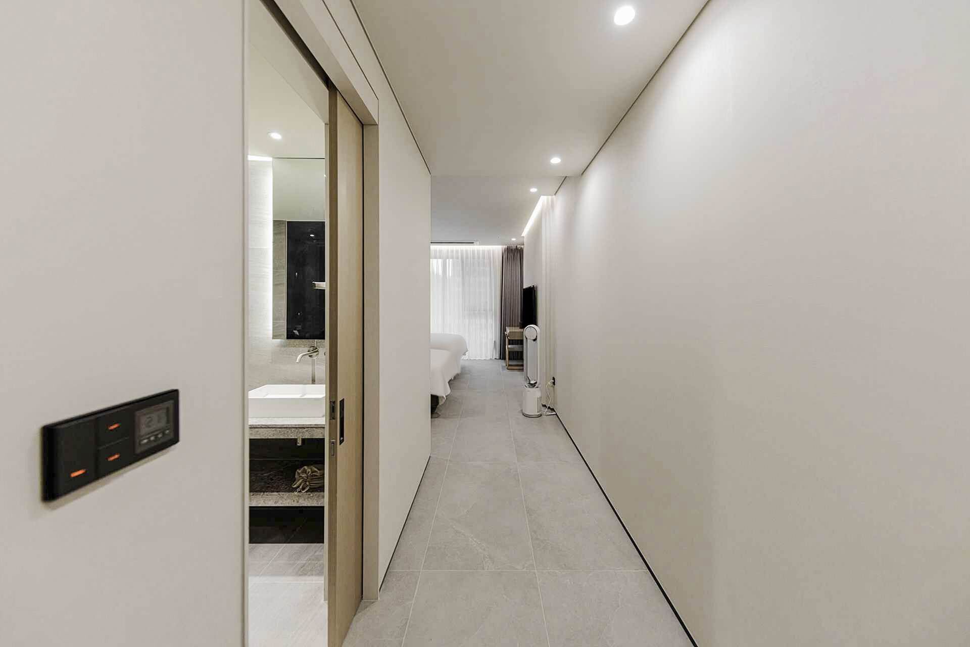 A modern hotel hallway with a digital control panel, a bathroom with a bathtub, and a bed with a TV.