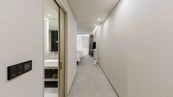 A modern hotel hallway with a digital control panel, a bathroom with a bathtub, and a bed with a TV.