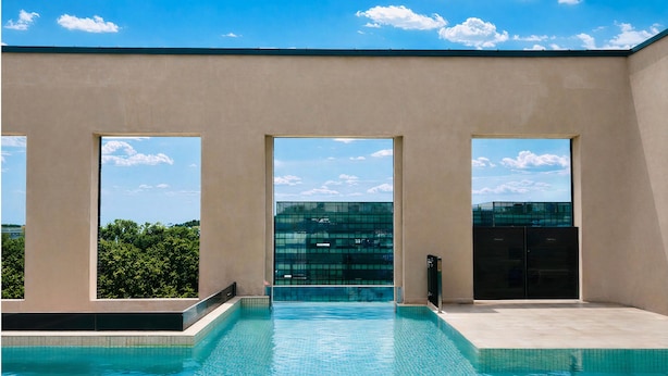 A swimming pool with clear blue water, large windows, and a view of a building and trees. - Daegu Suseong The Arco Hotel Lions Park (Daegu)