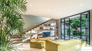 A modern living room with a staircase, a large window, and a plant. - Lane House 2 (Canggu)