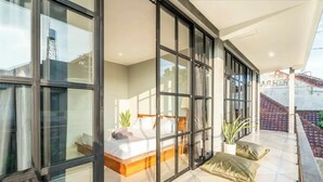 A modern bedroom with a large bed, a small table, and a potted plant. - Lane House 2 (Canggu)