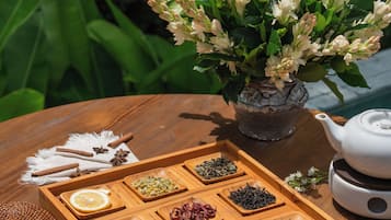 A wooden tray with tea and snacks, a white teapot, and a vase of flowers on a table outdoors.