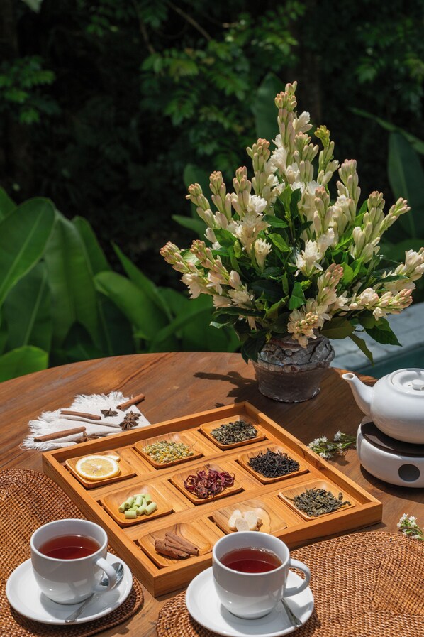 A wooden tray with tea and snacks, a white teapot, and a vase of flowers on a table outdoors. - Ubud Mas Glamping Luxury Tent (Mas)