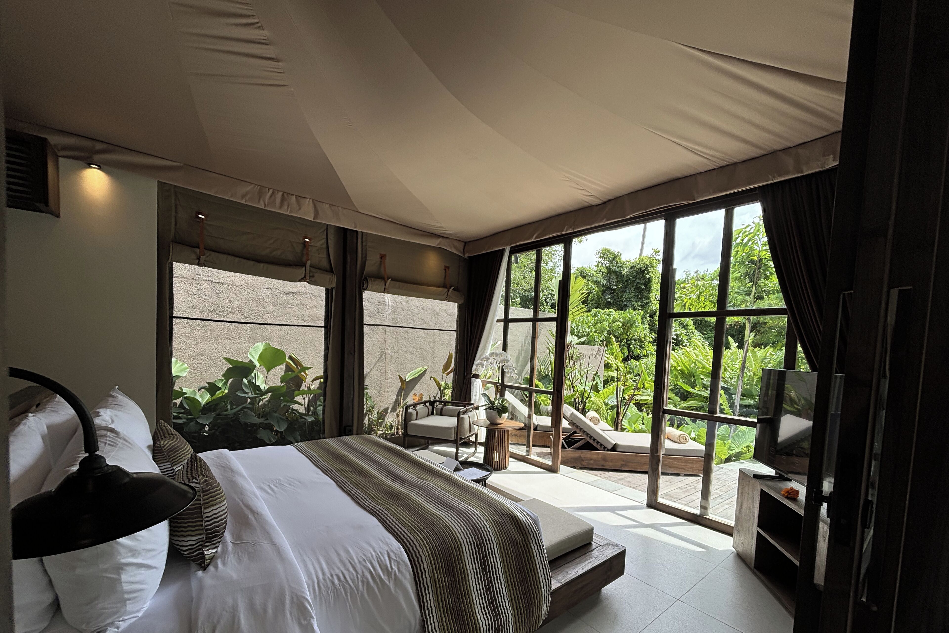 Ein Schlafzimmer mit einem großen Bett, einem Fernseher und Blick auf einen Garten durch eine Schiebetür.