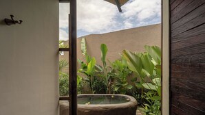 A stone hot tub in a garden with lush greenery and a wooden deck. - Ubud Mas Glamping Luxury Tent (Mas)