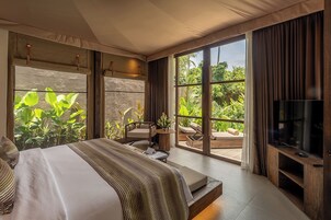 A spacious bedroom with a large bed, a TV, and a balcony with a view of lush greenery.