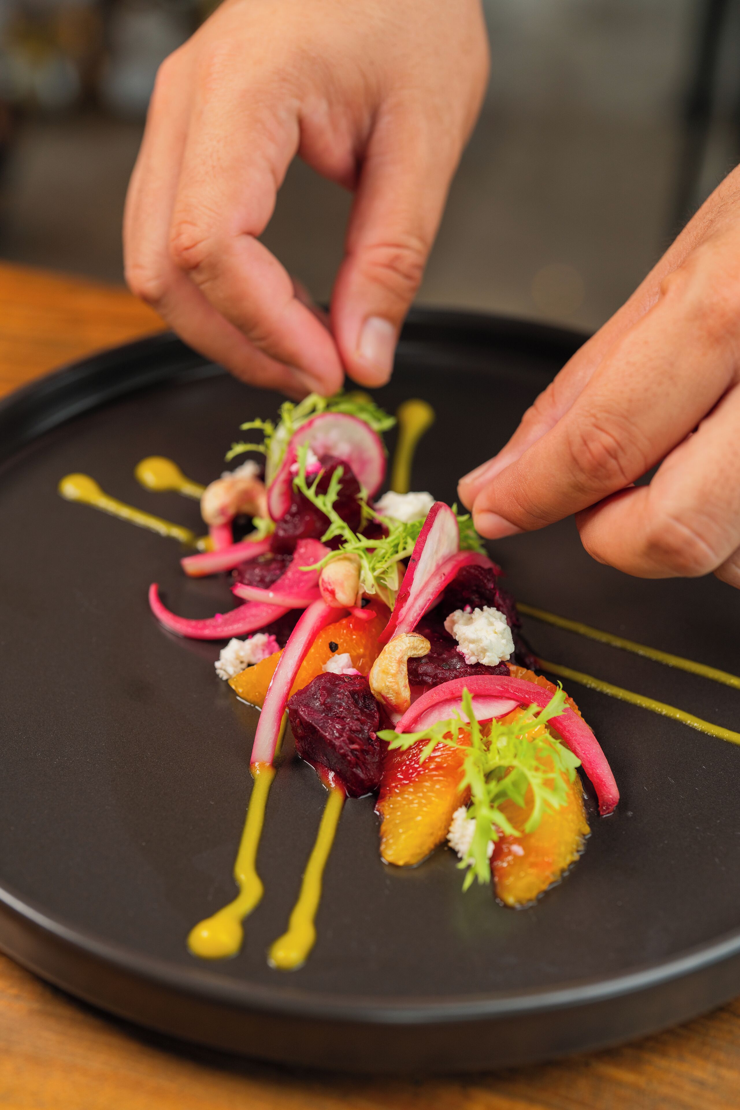 A chef's hands arranging a dish on a black plate.