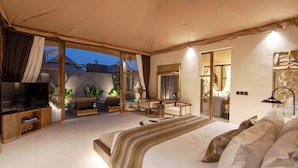 A spacious bedroom with a large bed, a TV, a desk, and a balcony with plants. - Ubud Mas Glamping Luxury Tent (Mas)