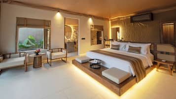 A modern bedroom with a large bed, a sofa, a small table, and a view of greenery outside.
