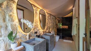 Baño con paredes de piedra, dos lavamanos y un espejo grande.