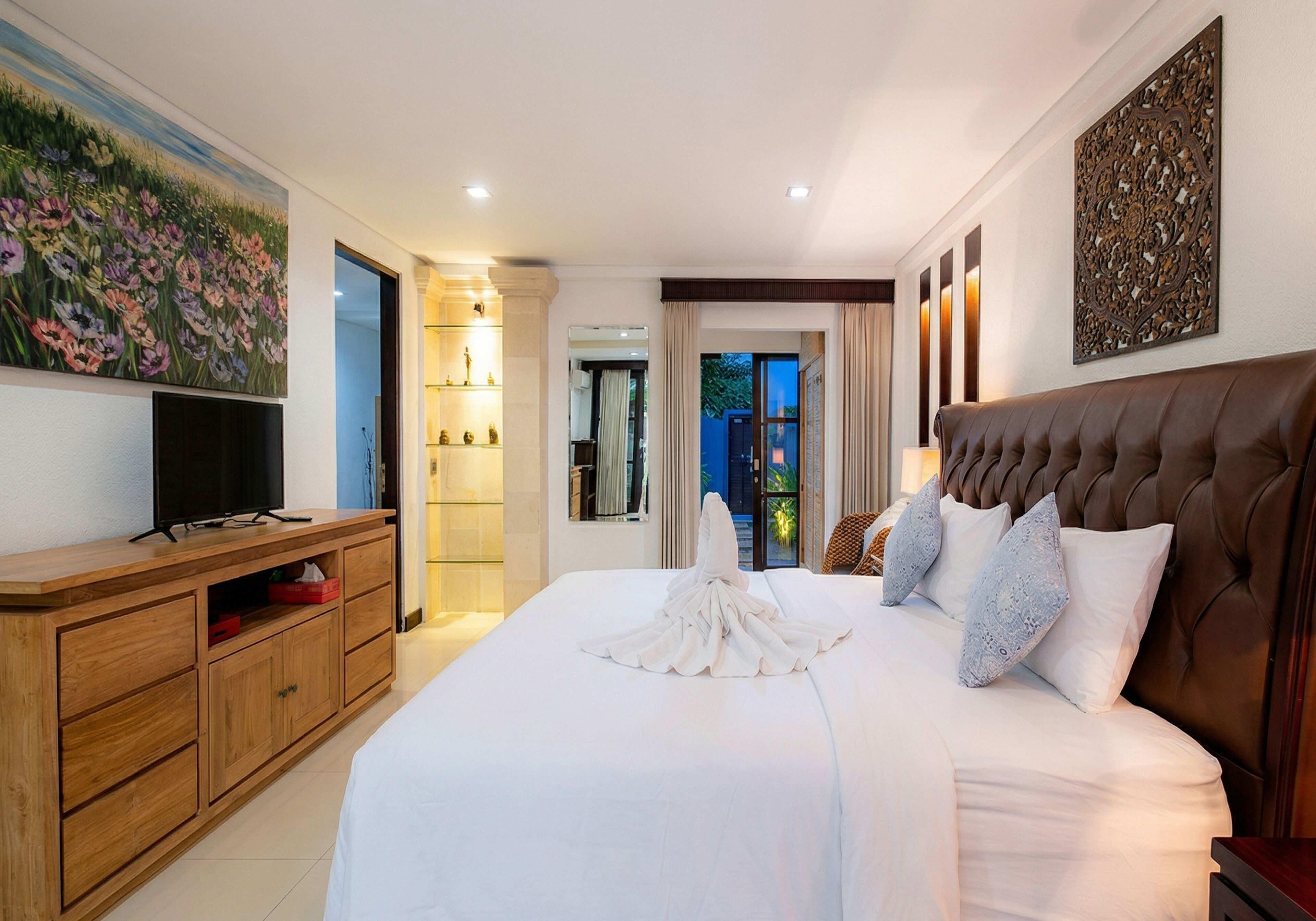 A hotel room with a large bed, a wooden dresser, a television, and a painting on the wall.