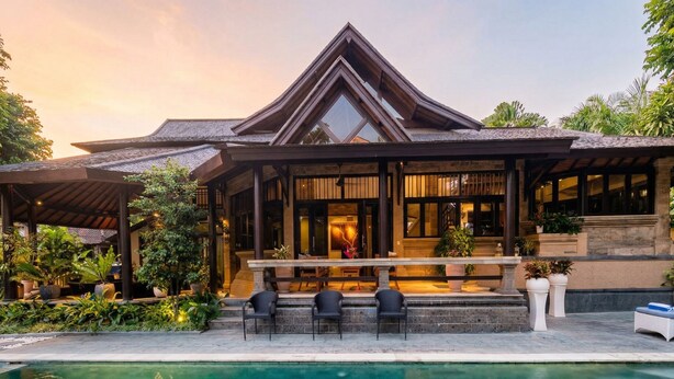 A resort with a pool, outdoor seating, and a large building with a triangular roof. - Villa Frangipani Seminyak (Seminyak)