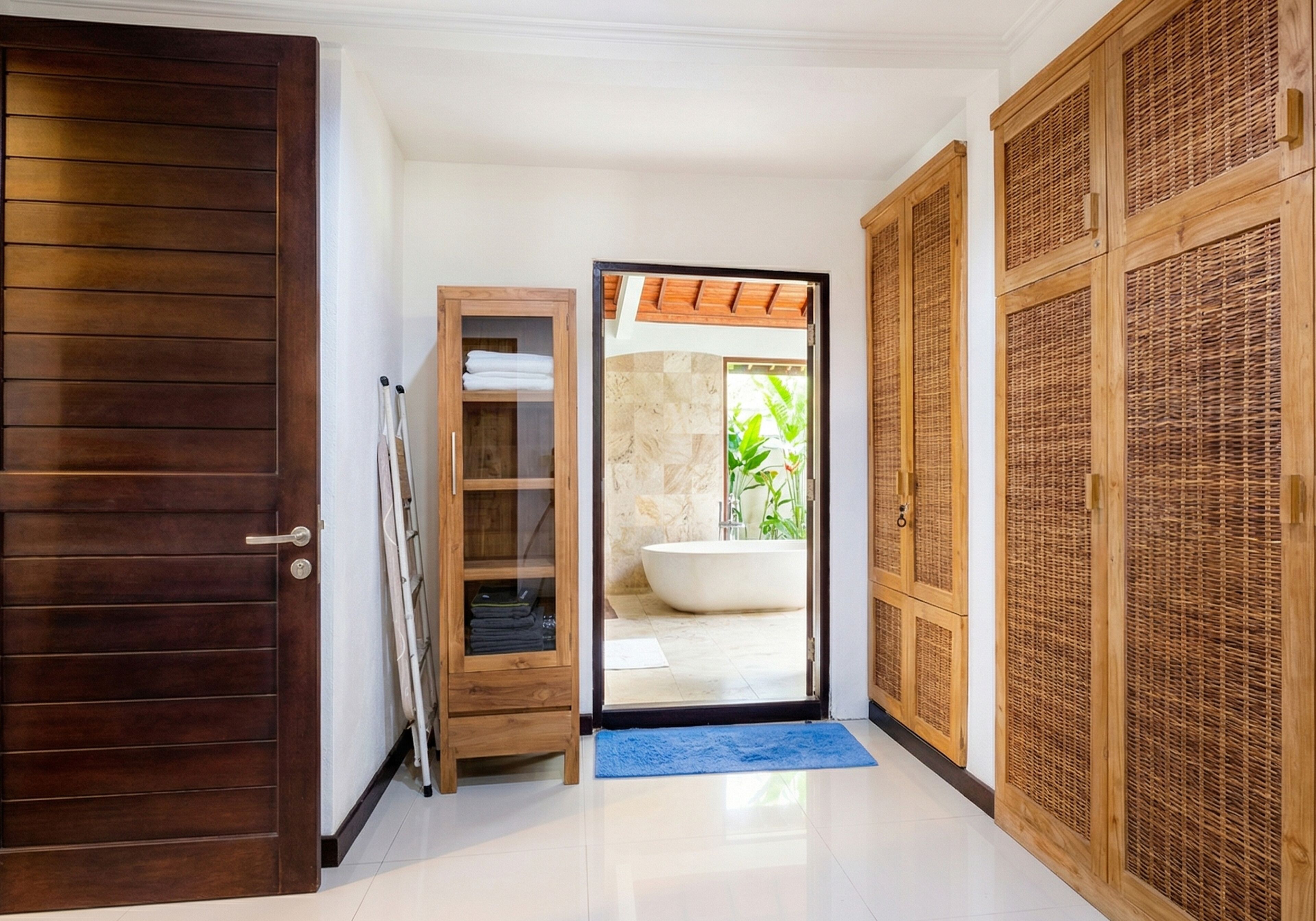 A bathroom with a bathtub, a wooden wardrobe, and a blue mat at the entrance.