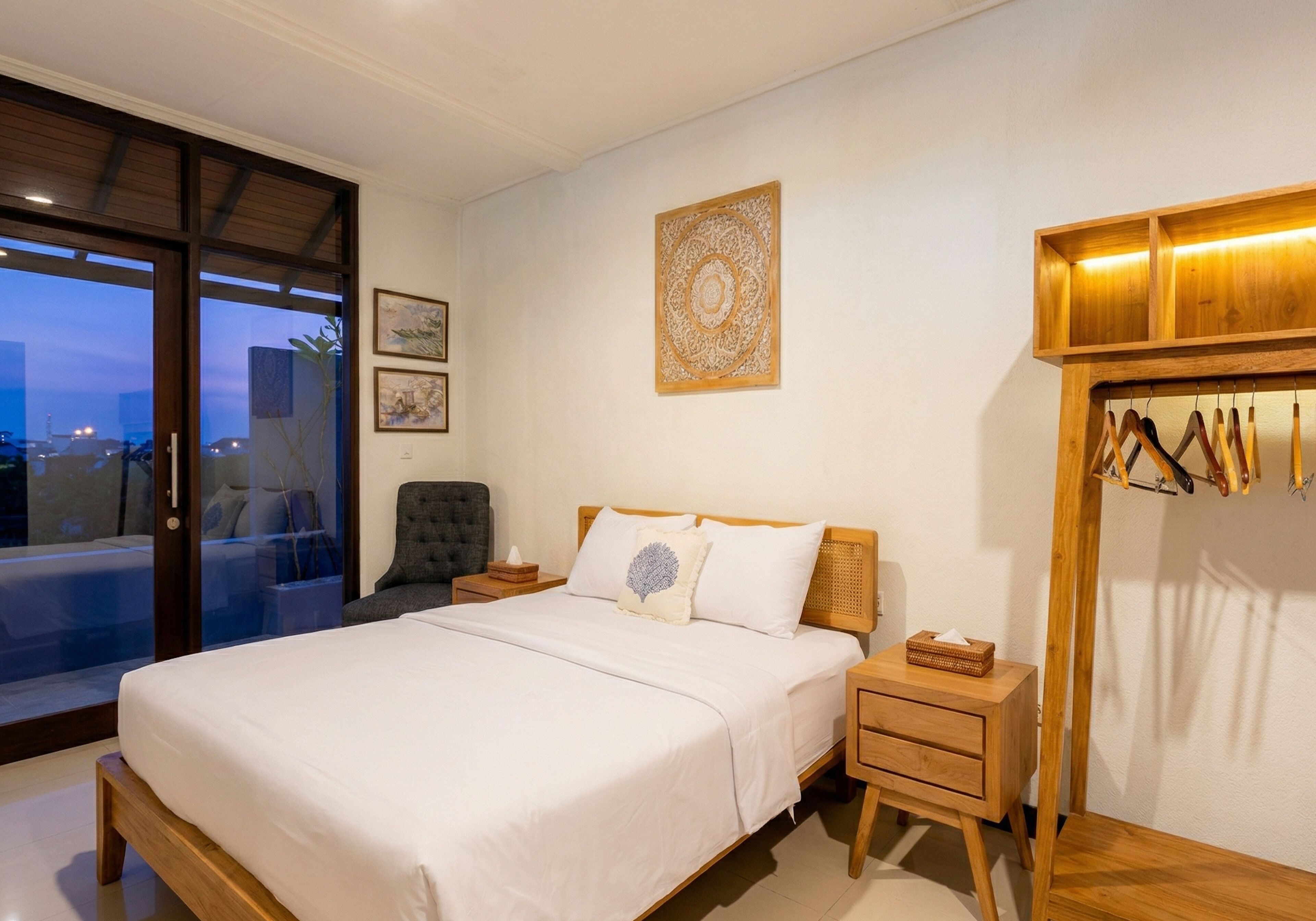A bedroom with a bed, nightstands, a chair, a wooden wardrobe, and a large window with a view.