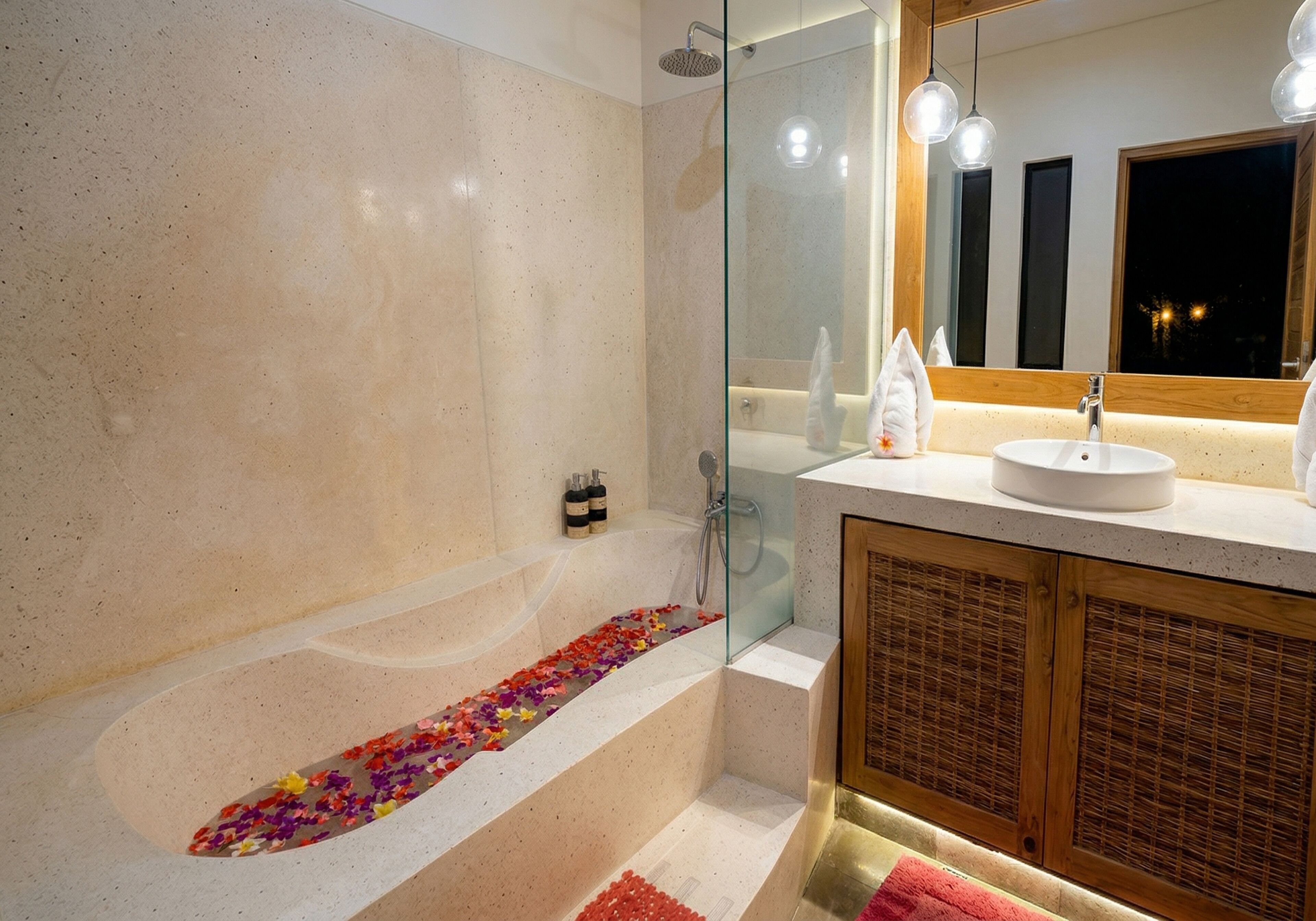 A modern bathroom with a glass-enclosed shower, a bathtub with flower petals, a wooden cabinet, and a large mirror.