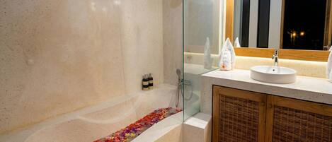 A modern bathroom with a glass-enclosed shower, a bathtub with flower petals, a wooden cabinet, and a large mirror.