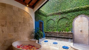 A spa area with a large bathtub, a shower, and a wall covered in greenery. - Villa Frangipani Seminyak (Seminyak)