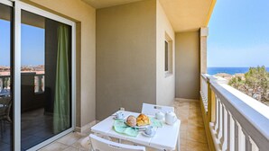 A balcony with a table set for breakfast, a view of the sea, and a sliding glass door leading to an indoor area. - La Perla by Interhome (El Médano)