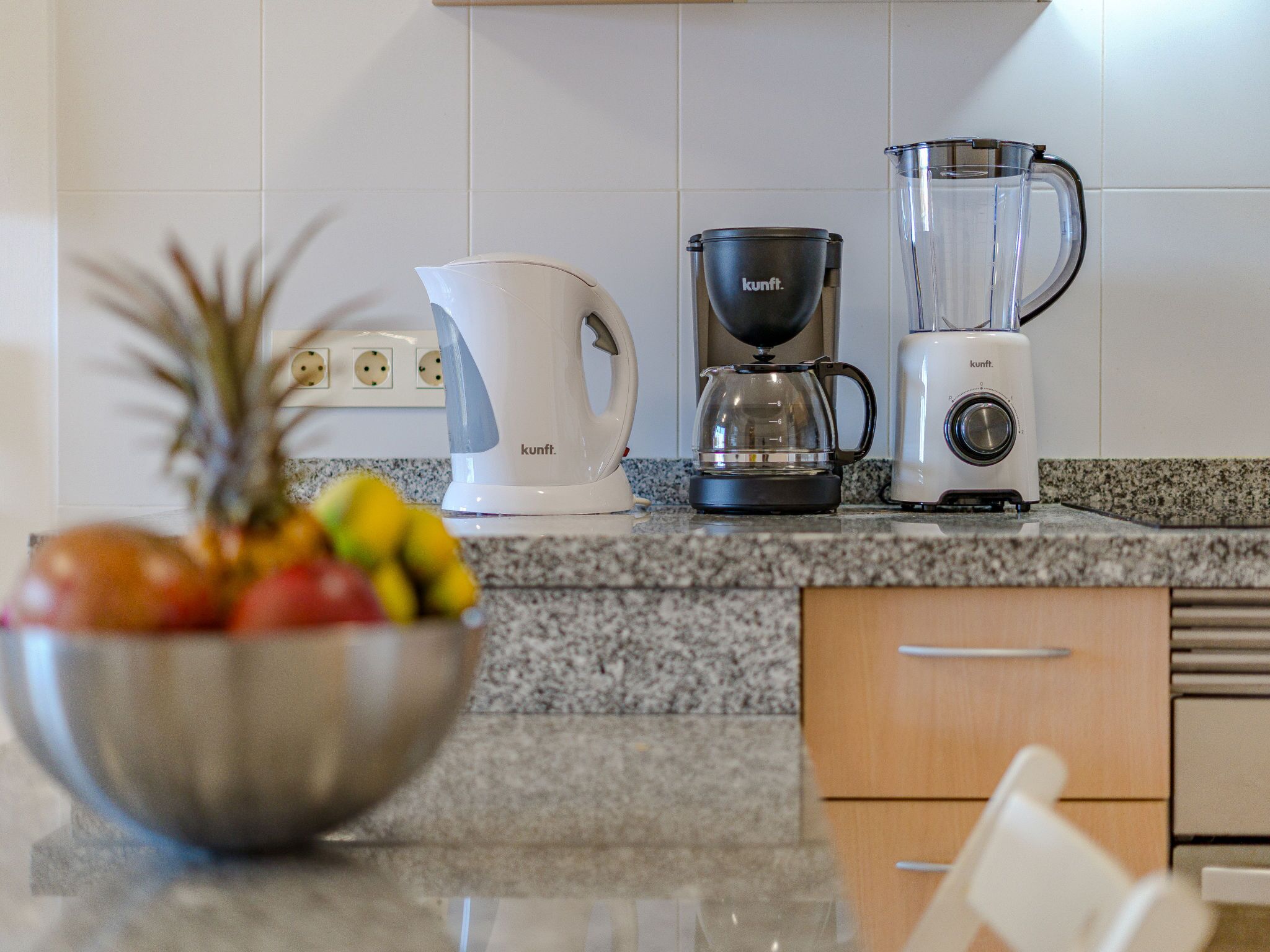 Una cucina con un piano di lavoro in granito, una macchina da caffè, un frullatore e una ciotola di frutta.
