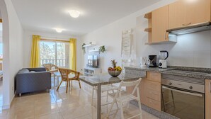 A modern kitchen with granite countertops, a built-in oven, and a coffee maker. There is a dining area with a gray sofa and wicker chairs. - La Perla by Interhome (El Médano)