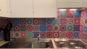 A kitchen with a stainless steel sink and stove, white cabinets, and colorful patterned tiles on the backsplash. - Alpine magic Leukerbad: Your dream holiday in the heart of the Swiss Alps (Leukerbad)