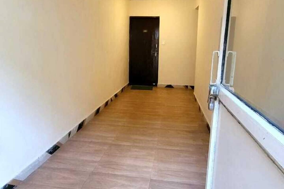 Un couloir étroit au sol en bois, aux murs blancs et à la porte noire au fond.