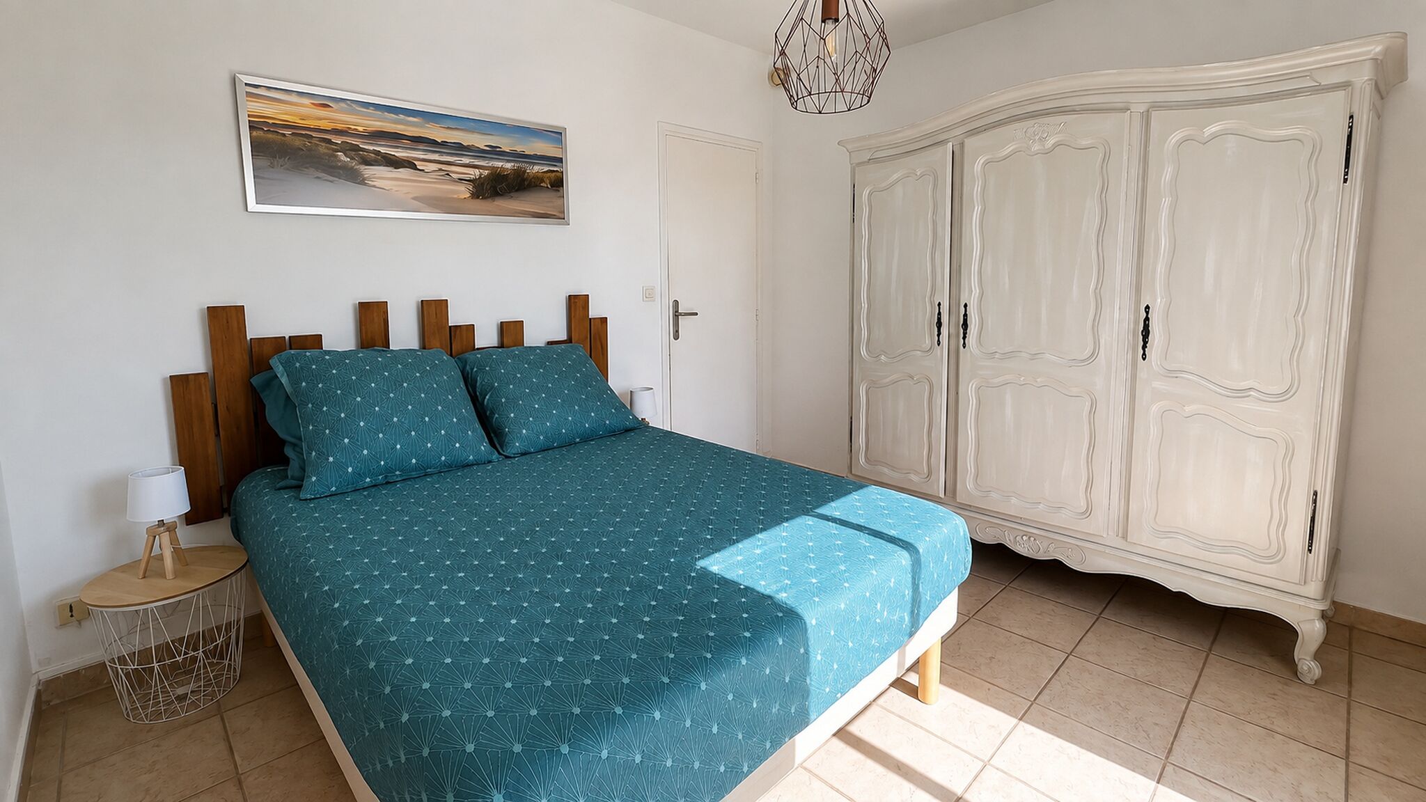 Ein Schlafzimmer mit Bett, Schrank, Nachttisch, Lampe und einem Bild an der Wand.