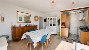 Een goed verlichte kamer met een eettafel, stoelen, een keukenhoek en een spiegel aan de muur.