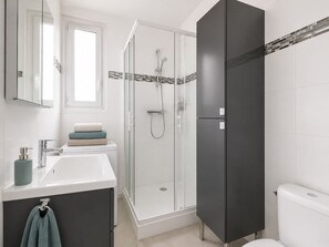 A modern bathroom with a glass shower enclosure, a white sink, and a dark-toned vanity.