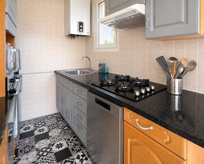 Una cocina moderna con estufa a gas, electrodomésticos de acero inoxidable, un fregadero y baldosas de suelo con diseño.
