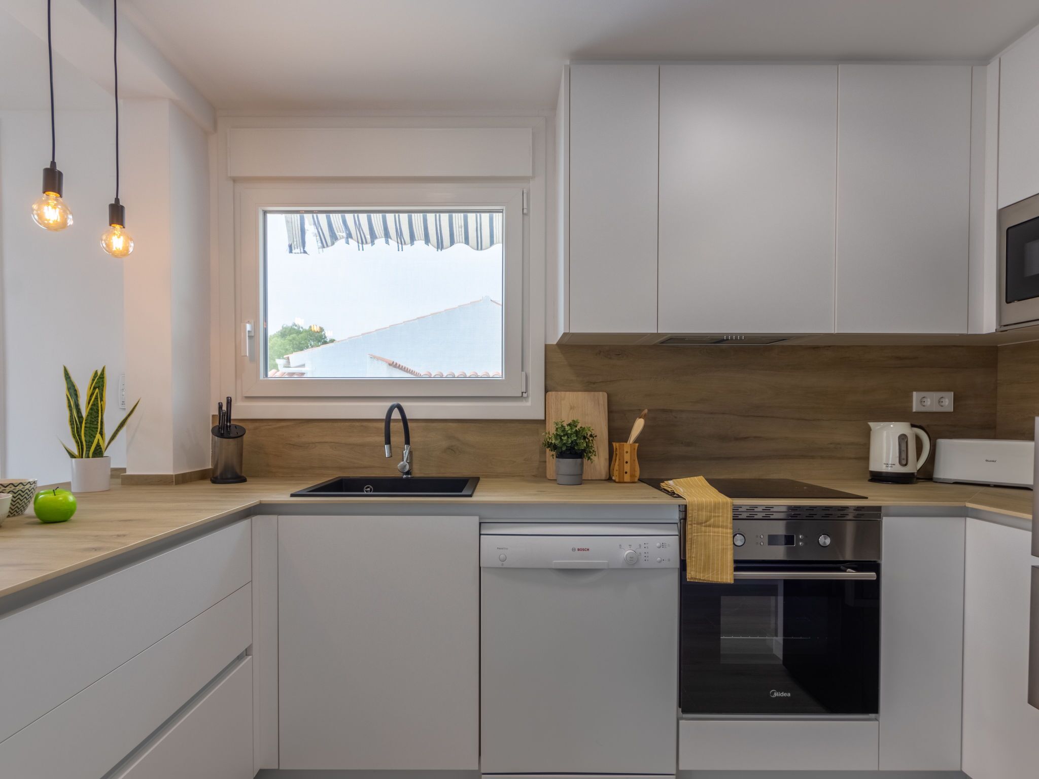 A modern kitchen with white cabinets, a Bosch dishwasher, a microwave, and a wooden countertop.