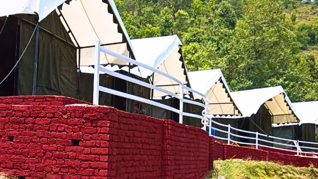 A row of tents with white awnings, a red brick wall, and a white fence.