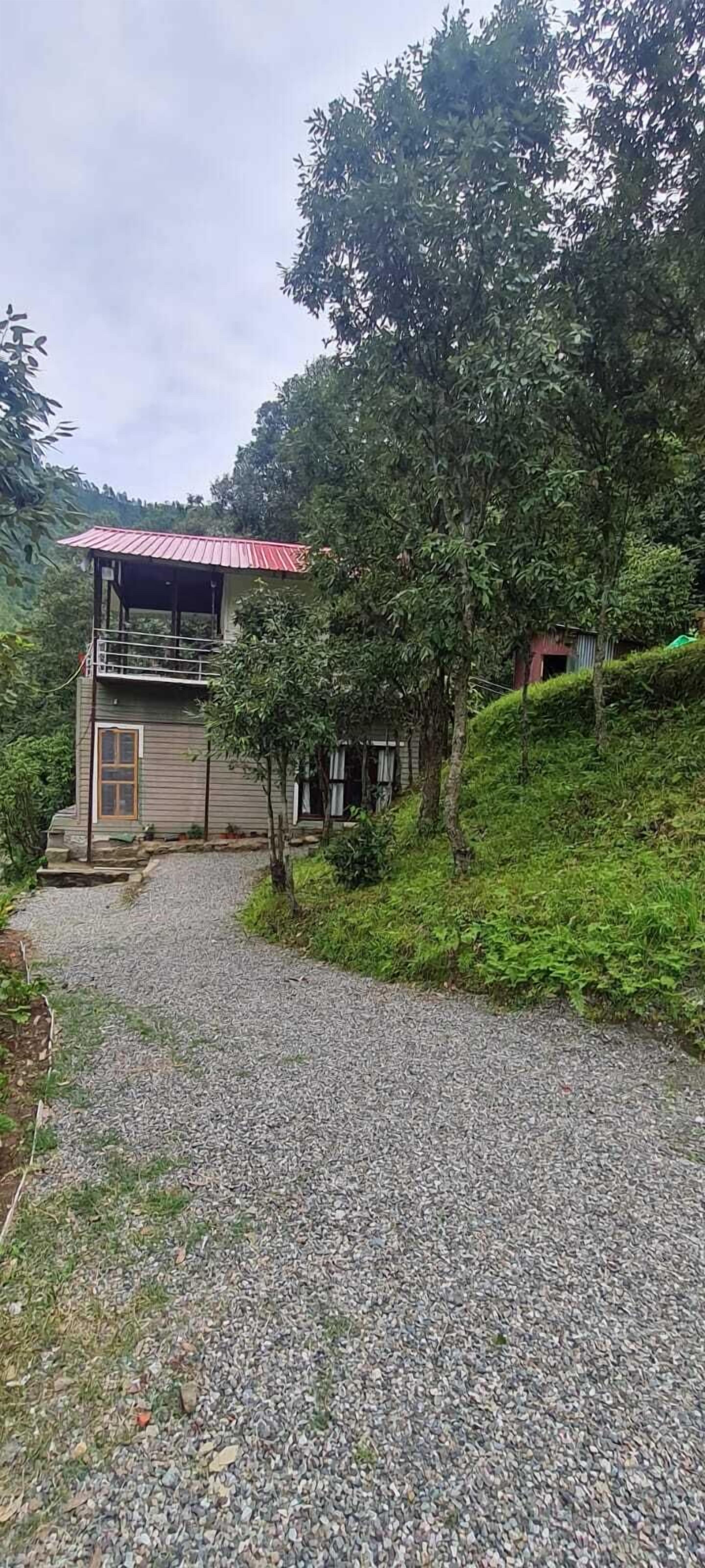 Un bâtiment à deux étages, doté d’un toit rouge, entouré d’une végétation luxuriante et accessible par un chemin de gravier menant à l’entrée.