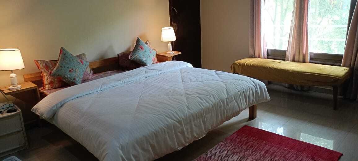 Un dormitorio con una cama grande, dos mesitas de noche con lámparas, un banco y una ventana con cortinas.