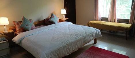 A bedroom with a large bed, two bedside tables with lamps, a bench, and a window with curtains.