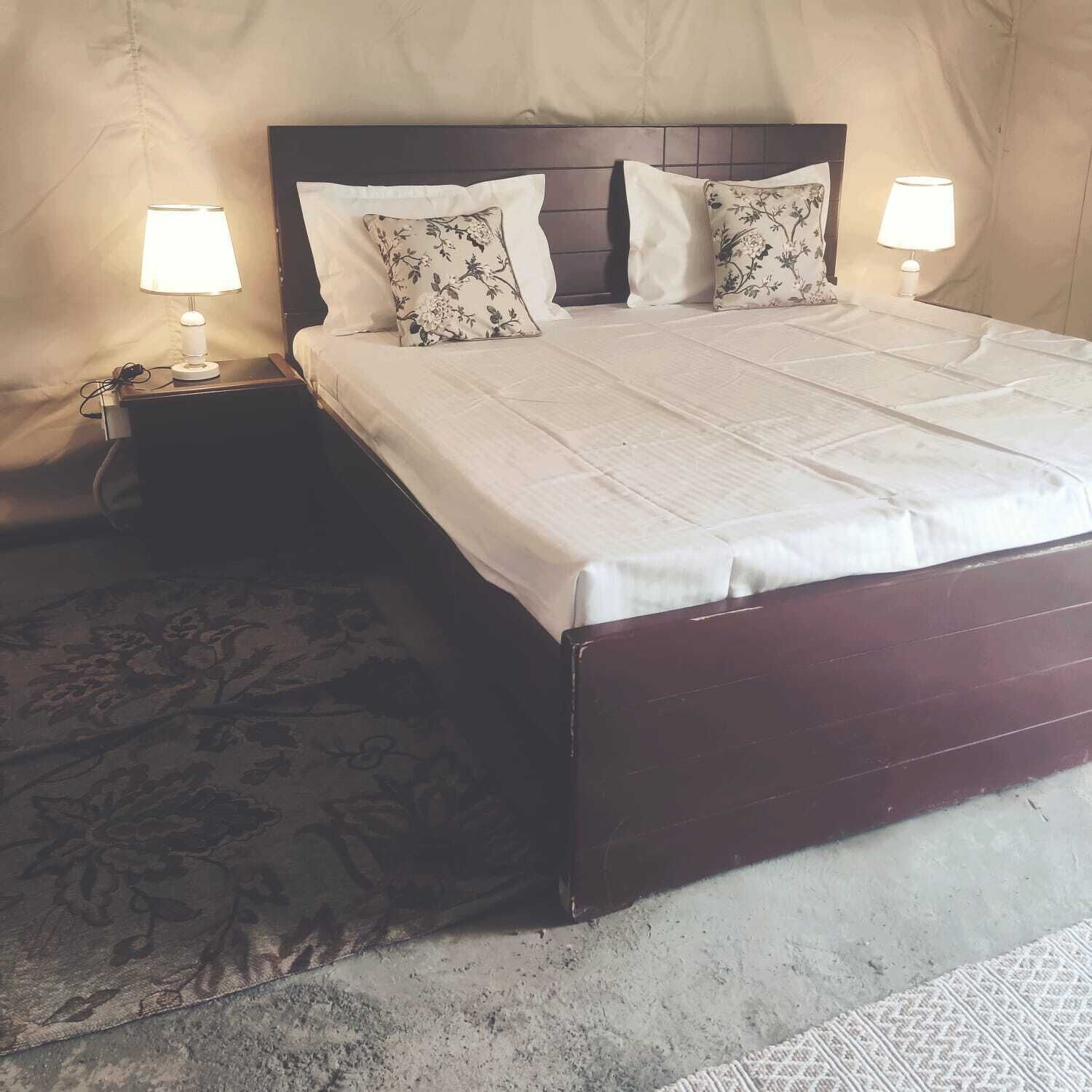A neatly made bed with floral-patterned pillows, a dark wooden headboard, and two bedside lamps on a textured rug.