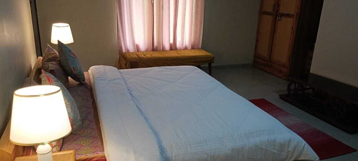 Habitación de hotel con cama, dos lámparas de noche, un banco, una ventana con cortinas y un armario.