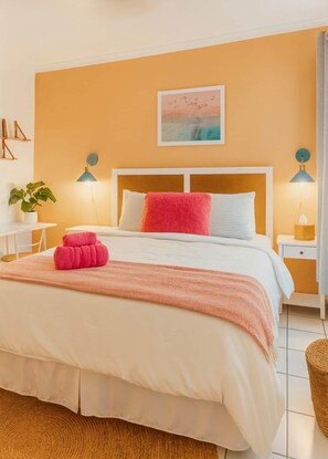 A neatly arranged bedroom with a bed, bedside tables, a lamp, a plant, and a painting on the wall. - The Catalina Beach Compound (Hollywood)