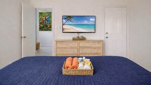 A bedroom with a bed, a television on the wall, a dresser, and a door.