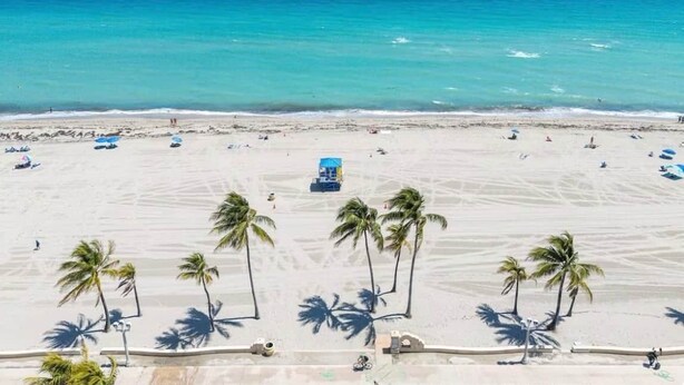 A beach with clear turquoise water, palm trees, and a few people.