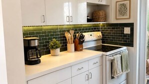 A kitchen with white cabinets, a stove, a coffee maker, and a green backsplash.