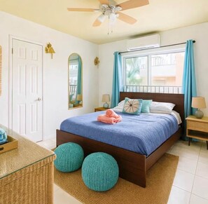 A bedroom with a bed, a ceiling fan, a window with curtains, a bedside table, and a nightstand.