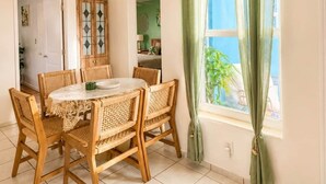 A dining area with a round table, wicker chairs, a wooden cabinet, and a window with green curtains.