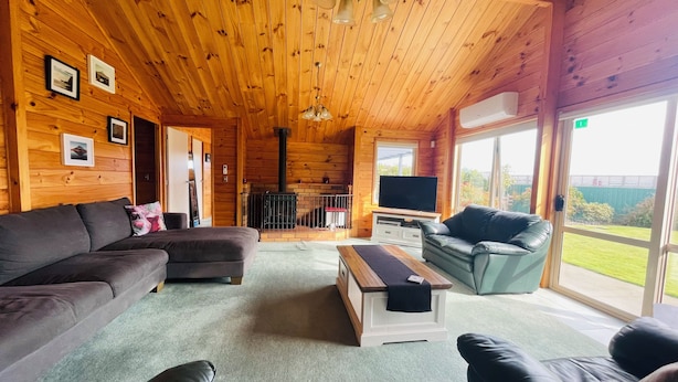 A cozy cabin interior with a wooden ceiling, a fireplace, a television, and a large window offering a view of the outdoors.