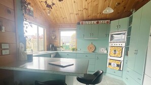 A kitchen with a wooden ceiling, a central island with stools, and a vintage oven.
